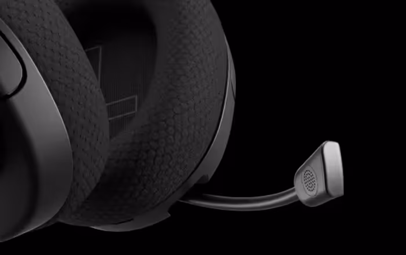 A close-up of a black gaming headset's textured earcup and flexible boom microphone, highlighting the honeycomb-patterned fabric against a solid black background.