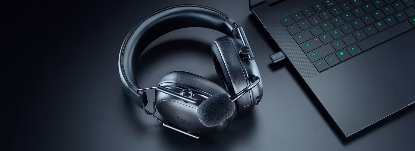 Wireless headset with microphone and a black laptop with green-backlit keyboard on a dark surface.