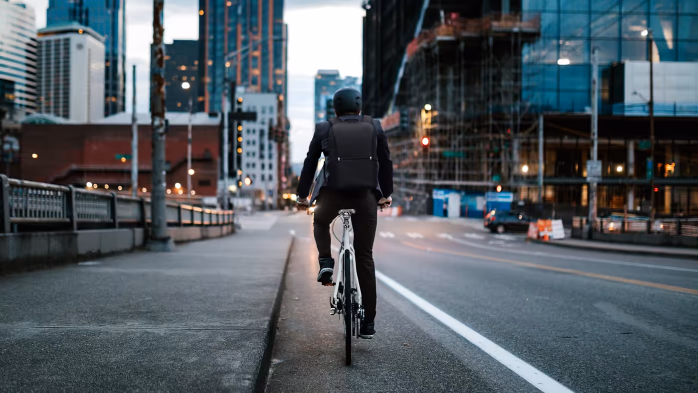 Man on a bicycle with the city in front of him wearing the reflective backpack