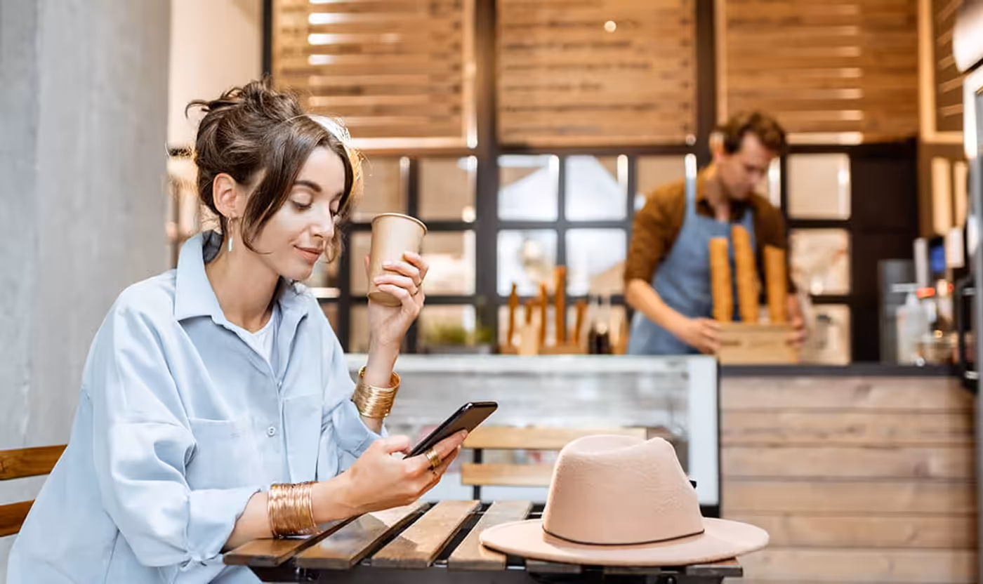 A customer using a smartphone at a cafe with the router owner nearby.