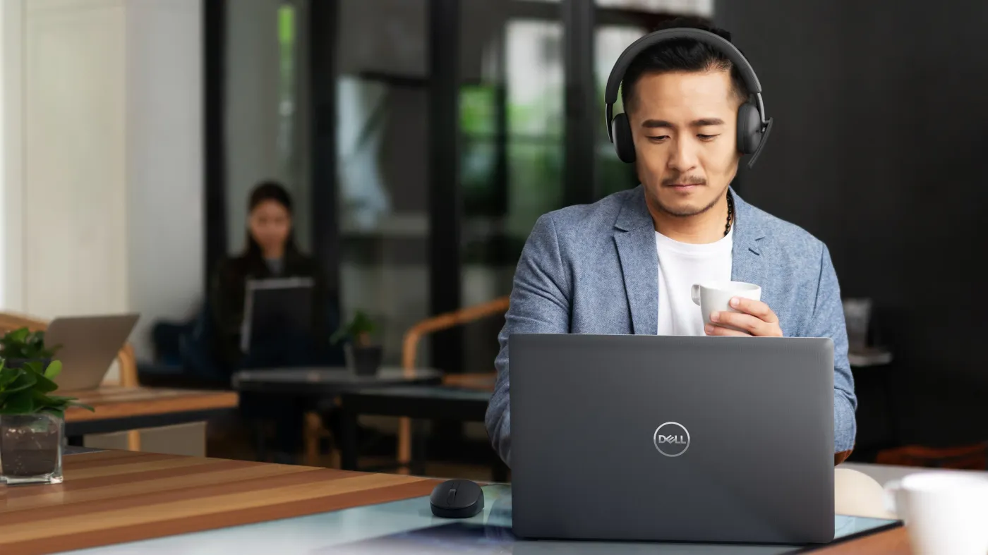 Man with headphones on his head using a Dell laptop on the table in front of him.