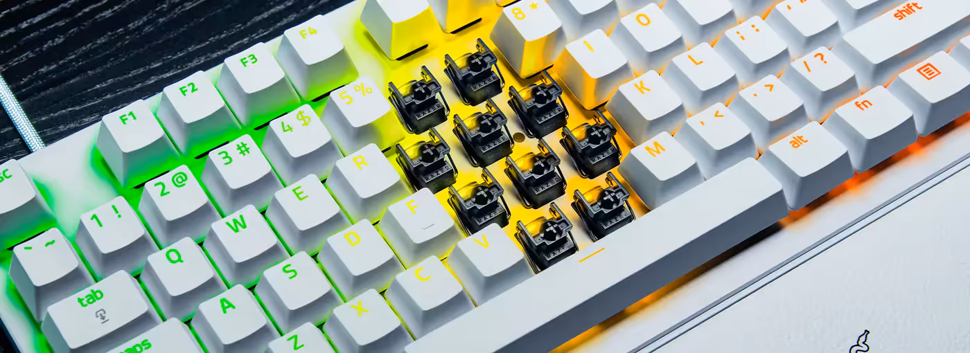 Keyboard with missing keycaps, revealing switches underneath, surrounded by RGB lighting in green, yellow, and orange hues.