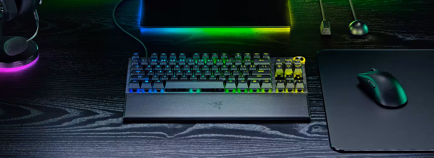 Gaming setup featuring a RGB mechanical keyboard, mouse on mat, microphone, headset, and monitor on a black desk.