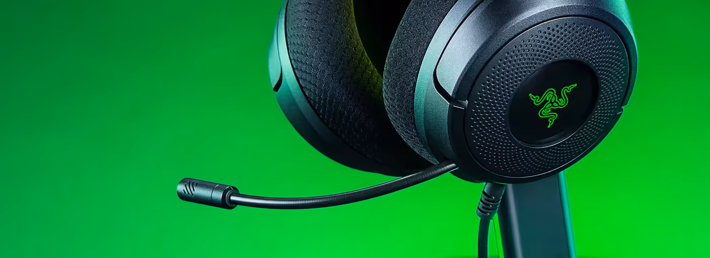 Close-up of Razer gaming headset with mic on black stand against green background, showing the Razer logo on earcup.