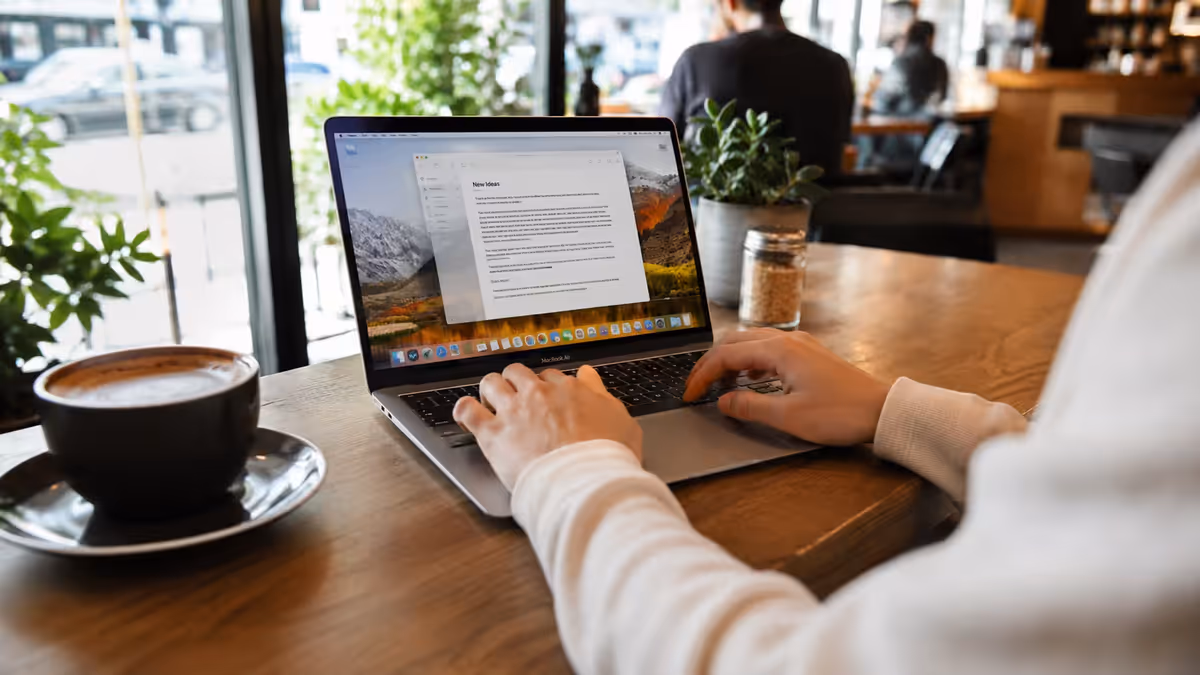 Lifestyle shot — Person typing on a MacBook Air at a Cape Town or Joburg café, natural light, coffee cup, no other distractions.