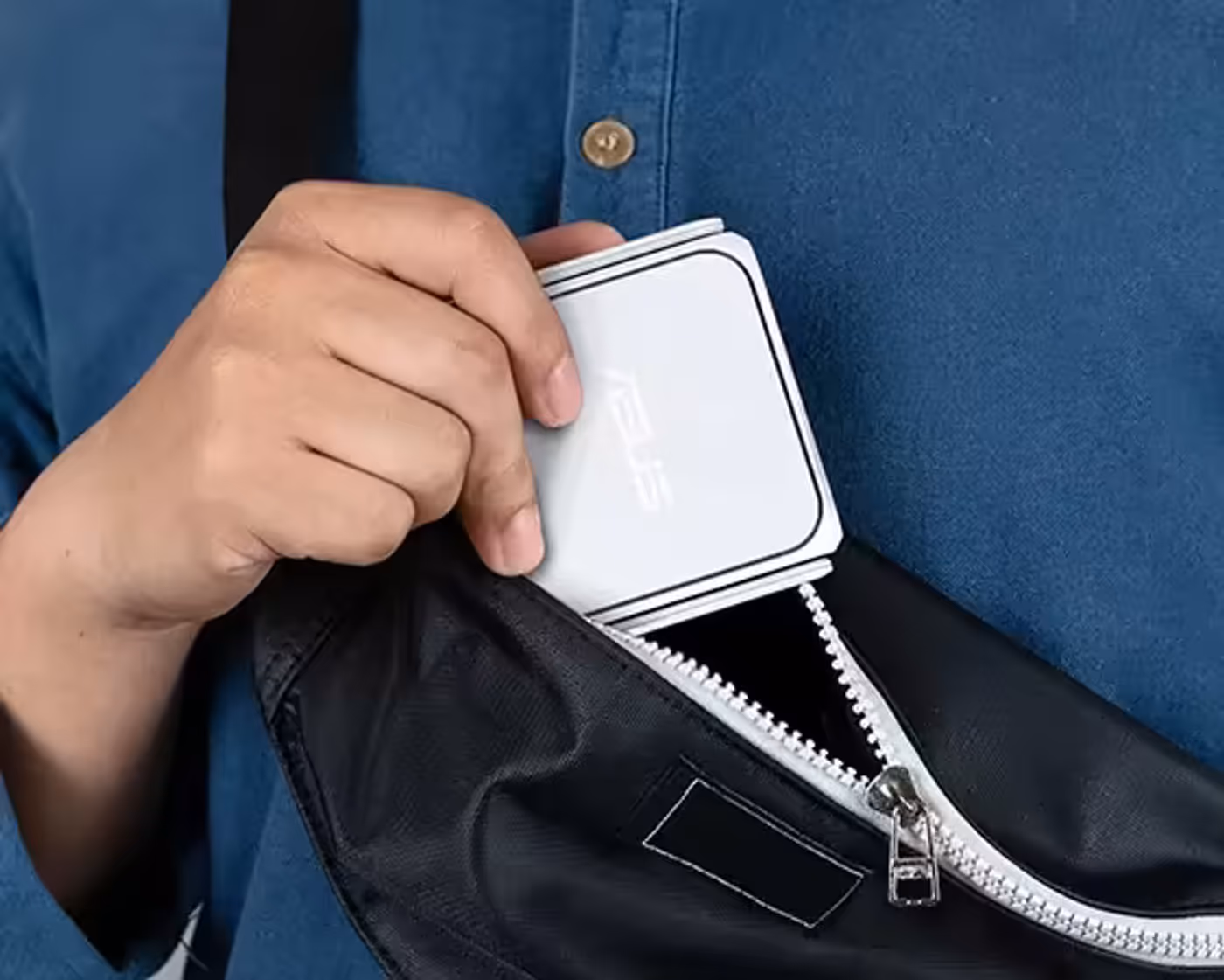 A hand placing the RT-BE58 Go into a crossbody bag, showing its portable design.