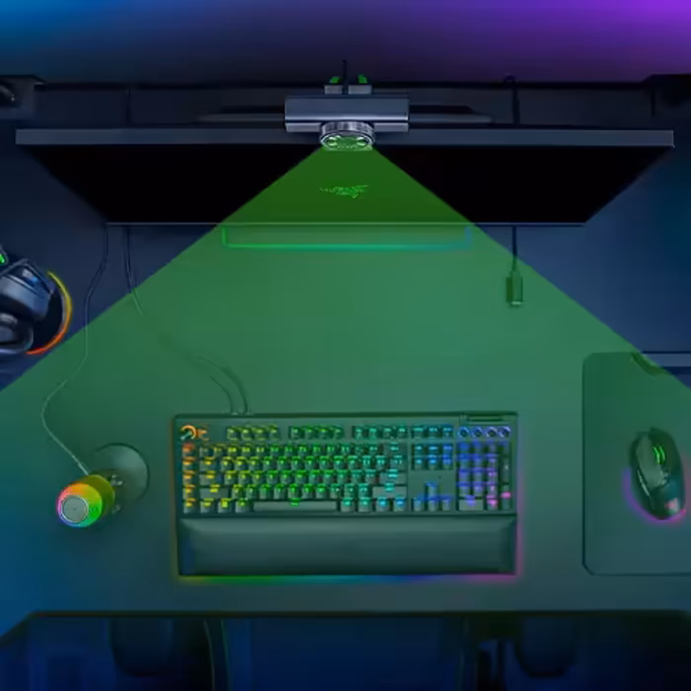A gaming setup with a keyboard backlit in rainbow colors, a mouse, a pair of headphones, a coffee mug, and a monitor emitting a green laser light.